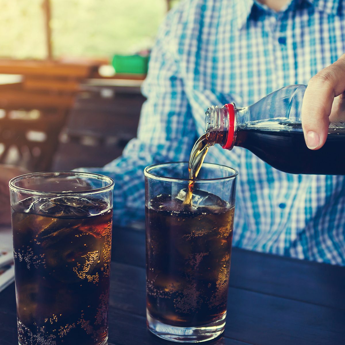 Women hand pour or fill drink in glass, double glass of soda on wooden table