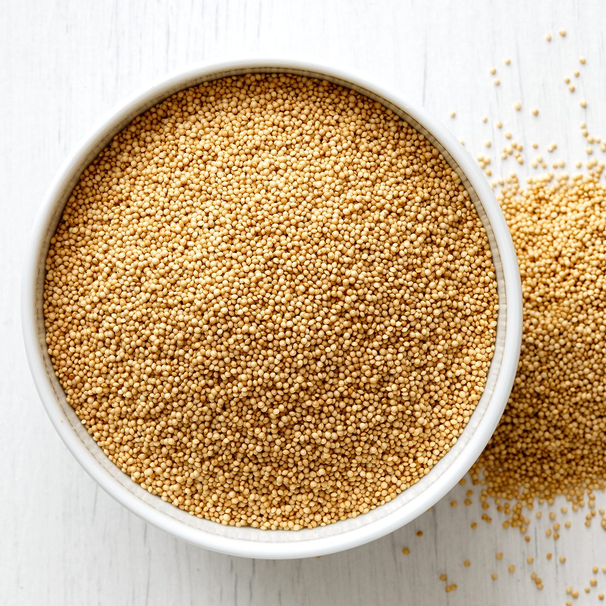 Amaranth seeds in white ceramic bowl isolated on painted white wood from above.