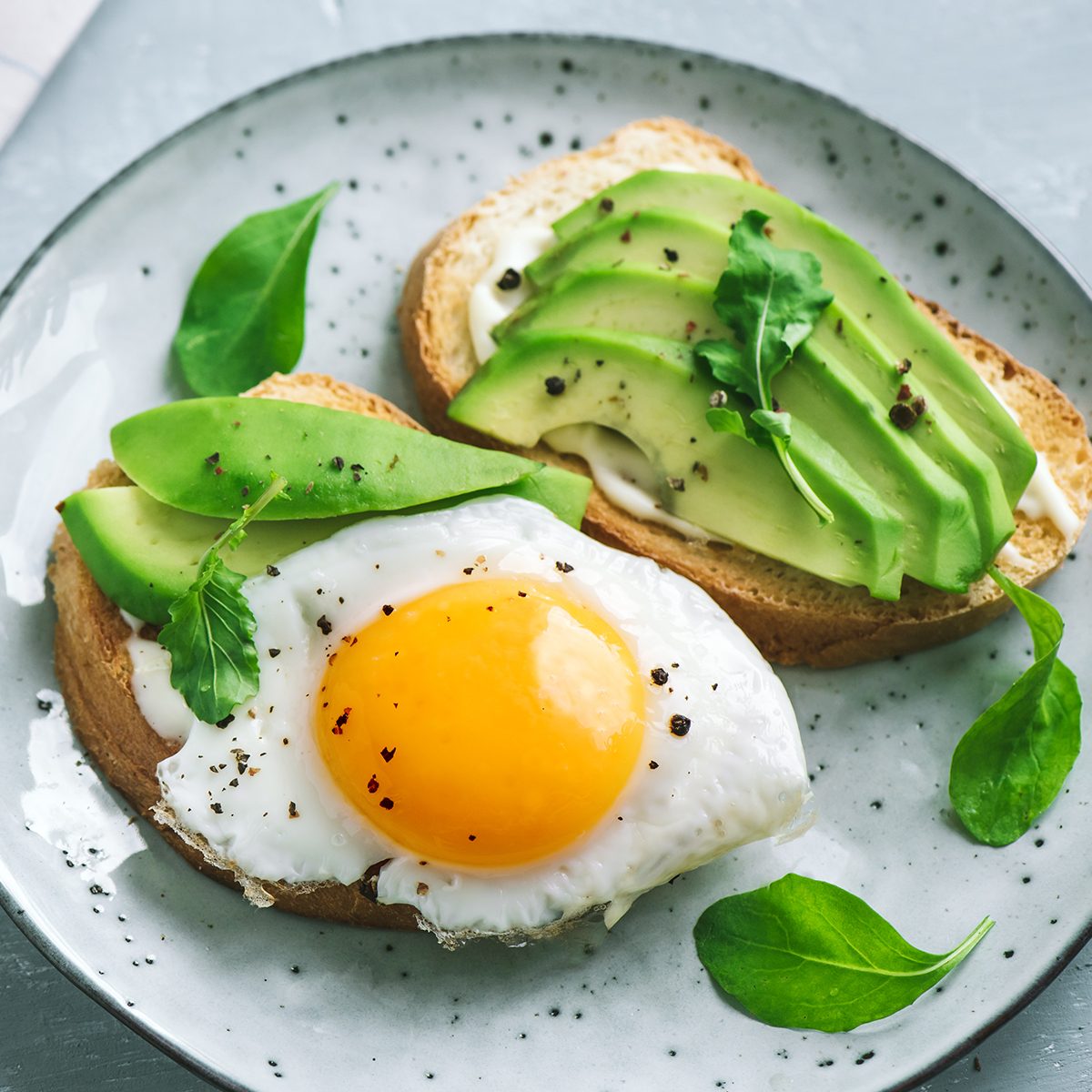 Avocado Sandwich with Fried Egg - sliced avocado and egg on toasted bread with arugula for healthy breakfast or snack.