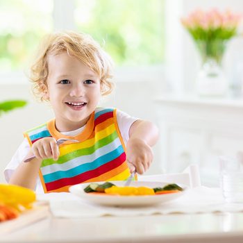 Child eating vegetables sitting in white high chair.