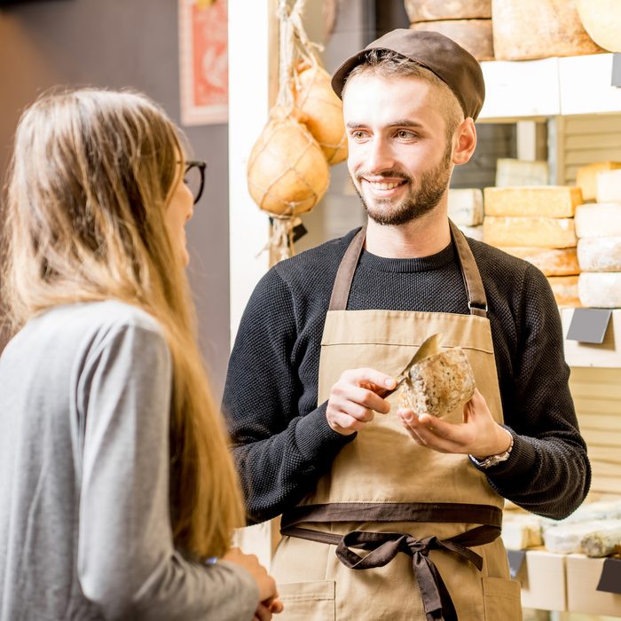 Salesman with a woman customer choosing a cheese for buying at the food store