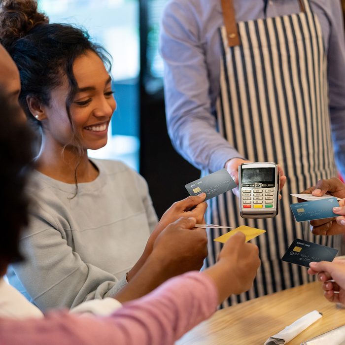 Happy group of friends paying with a credit card at a restaurant and splitting the bill – business concepts. **DESIGN ON CARDS WERE MADE FROM SCRATCH BY US**