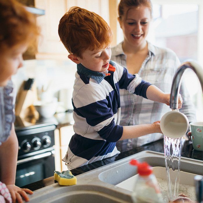 Two children and their Mother washing the dishes in the kitchen sink.