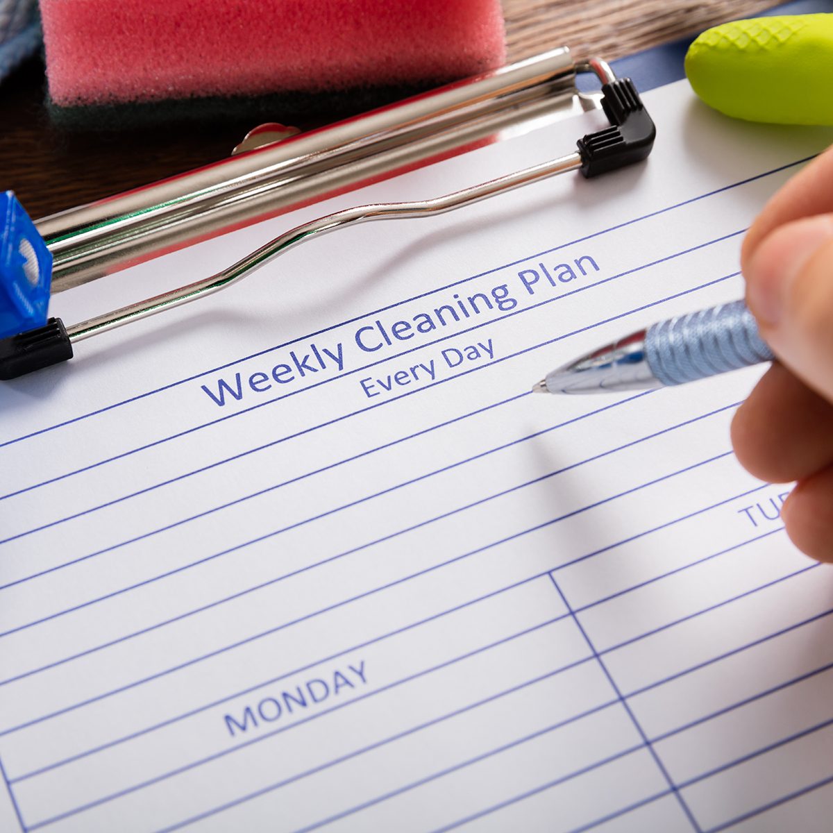 Close-up Of Person Hand Filling Weekly Cleaning Plan Form With Pen