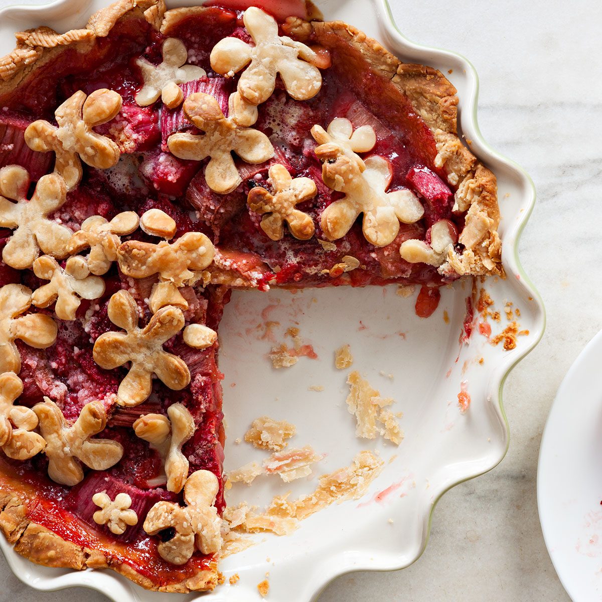 An overhead close up shot of a strawberry rhubarb pie and a slice.