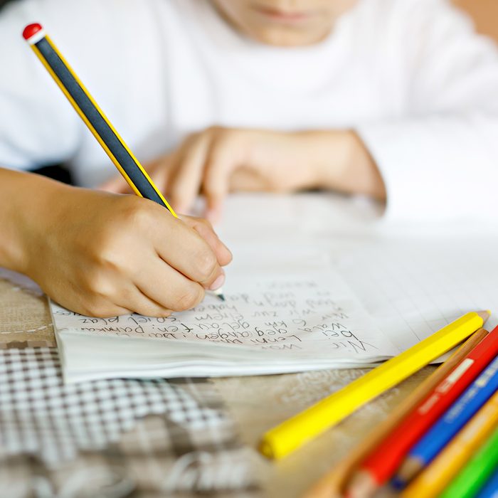 Child doing homework and writing story essay. Elementary or primary school class. Closeup of hands and colorful pencils.