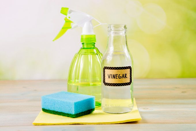 Chemical free home cleaner products concept. Using natural destilled white vinegar in spray bottle to remove stains. Tools on wooden table, green bokeh background, copy space.