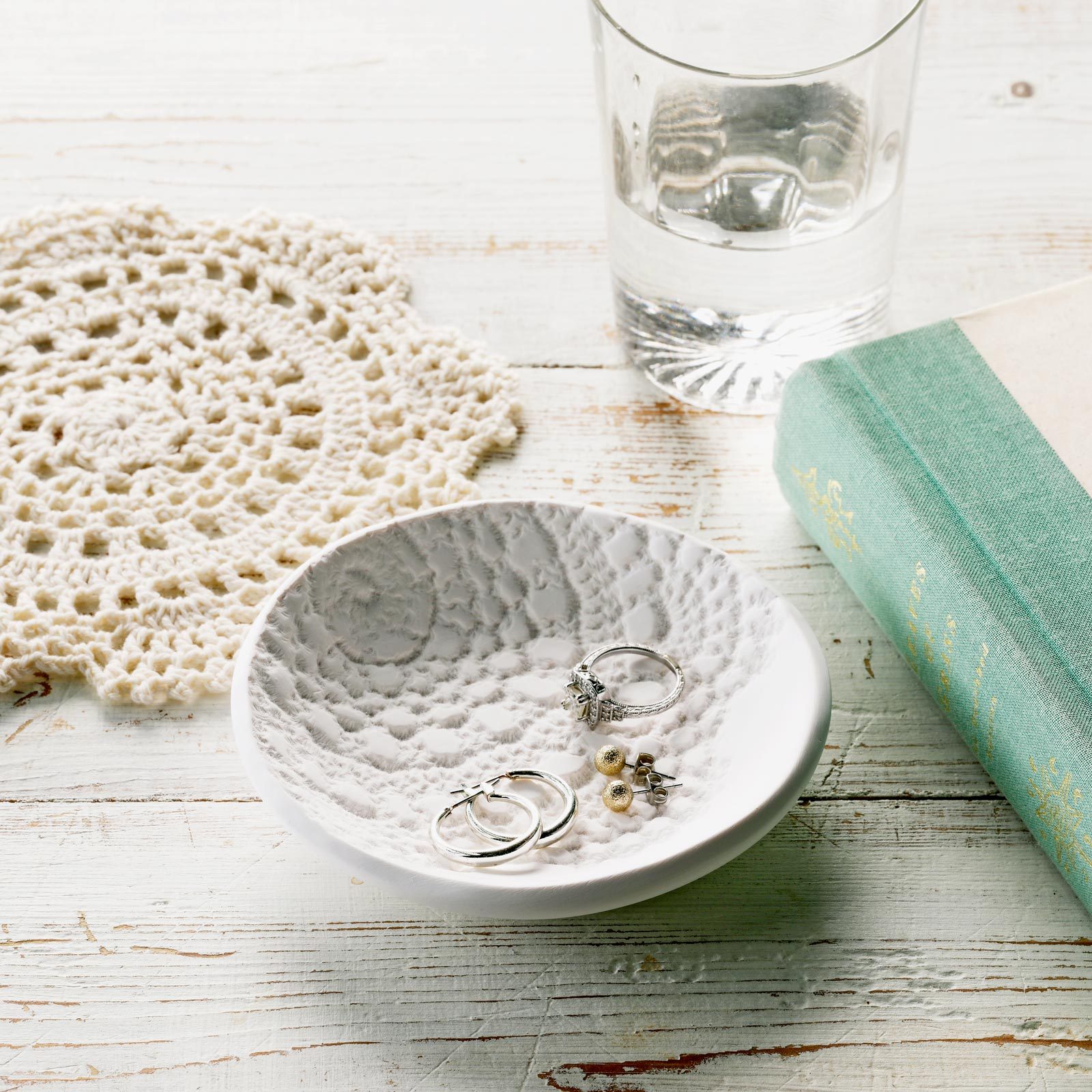 polymer clay lace dish holding jewelry with a glass of water, doily and book in the background