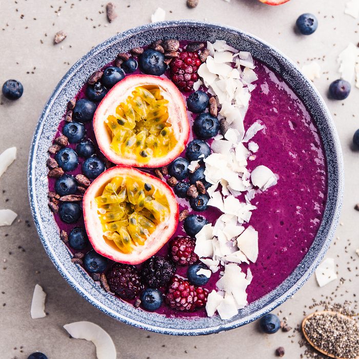 Tasty appetizing smoothie acai bowl made from blackberries and wild berries, decorated with cut passion fruit, coconut flakes, and cacao nibs. Served in bowl. Healthy life clean eating concept.
