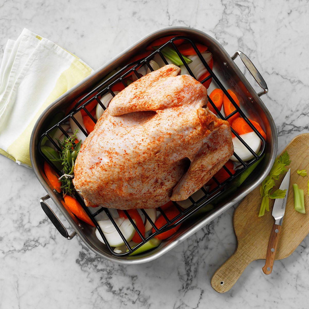 raw turkey with seasoning on a pan with vegetables underneath