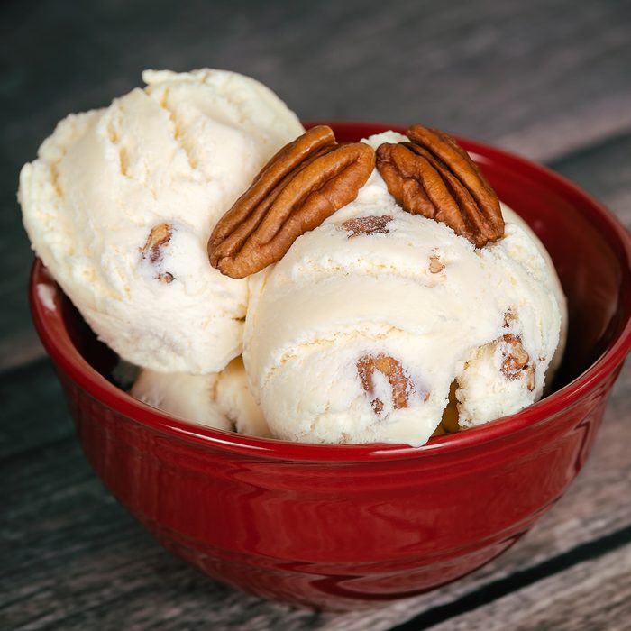 Delicious butter pecan ice cream served in a red bowl. Vintage wooden table background.