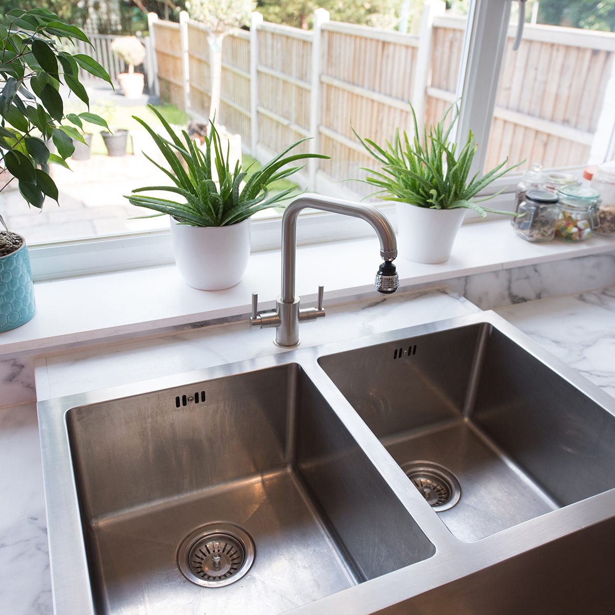 A general view of a kitchen interior with a modern stainless steel twin sinks by a window with a view into the garden