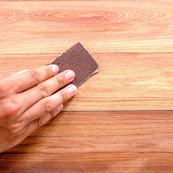 Cropped Hand Using Sand Paper On Wooden Table