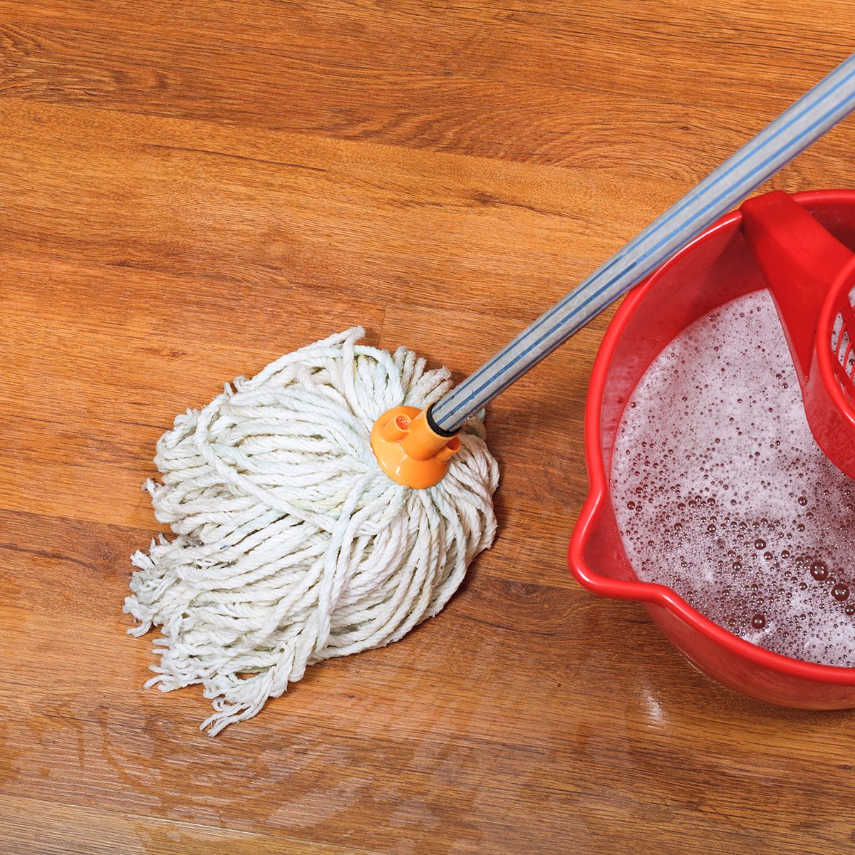 textile mop and red bucket on wooden wet floor