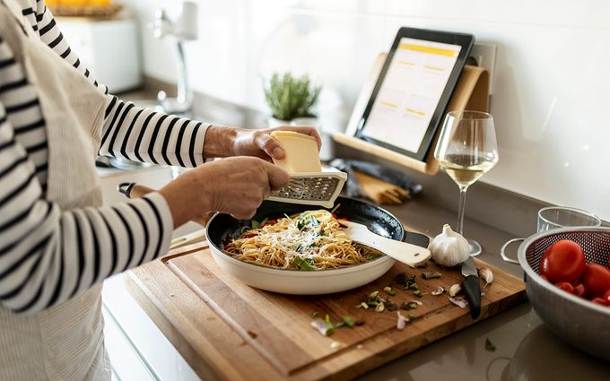 Close-up of woman with tablet cooking pasta dish in kitchen at home