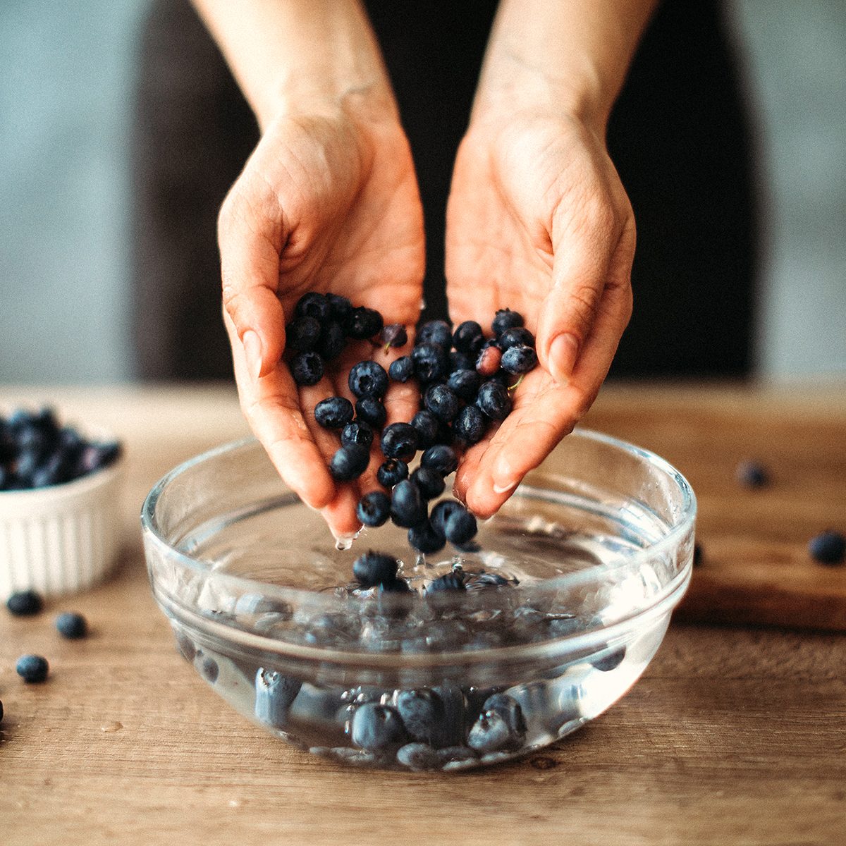 how to wash berries Unrecognizable woman cleaning blueberries in bowl with water on kitchen counter