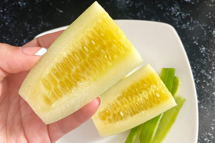 Yellow Cucumber sliced open being held over a white plate on a black countertop