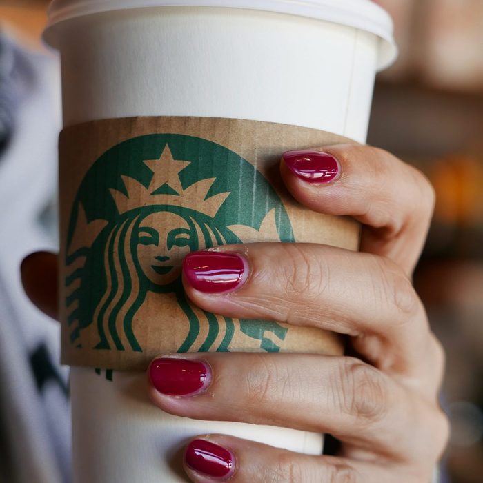 Hand holding a coffee cup in a Starbucks coffee shop. In...