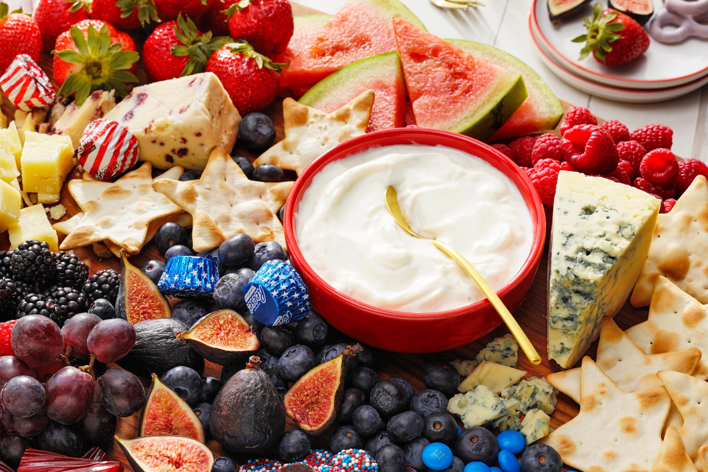 close up of dip in the middle of a fourth of july themed charcuterie board with red white and blue fruits and cheese