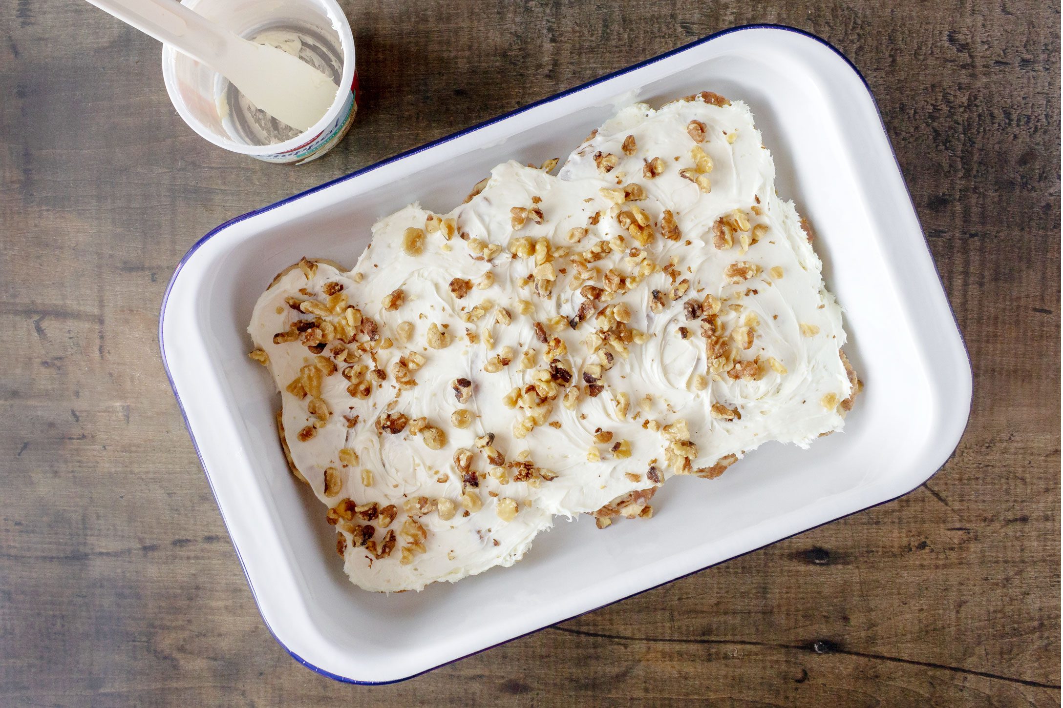 frosting and nuts on top of a pan filled with cinnamon rolls before baking