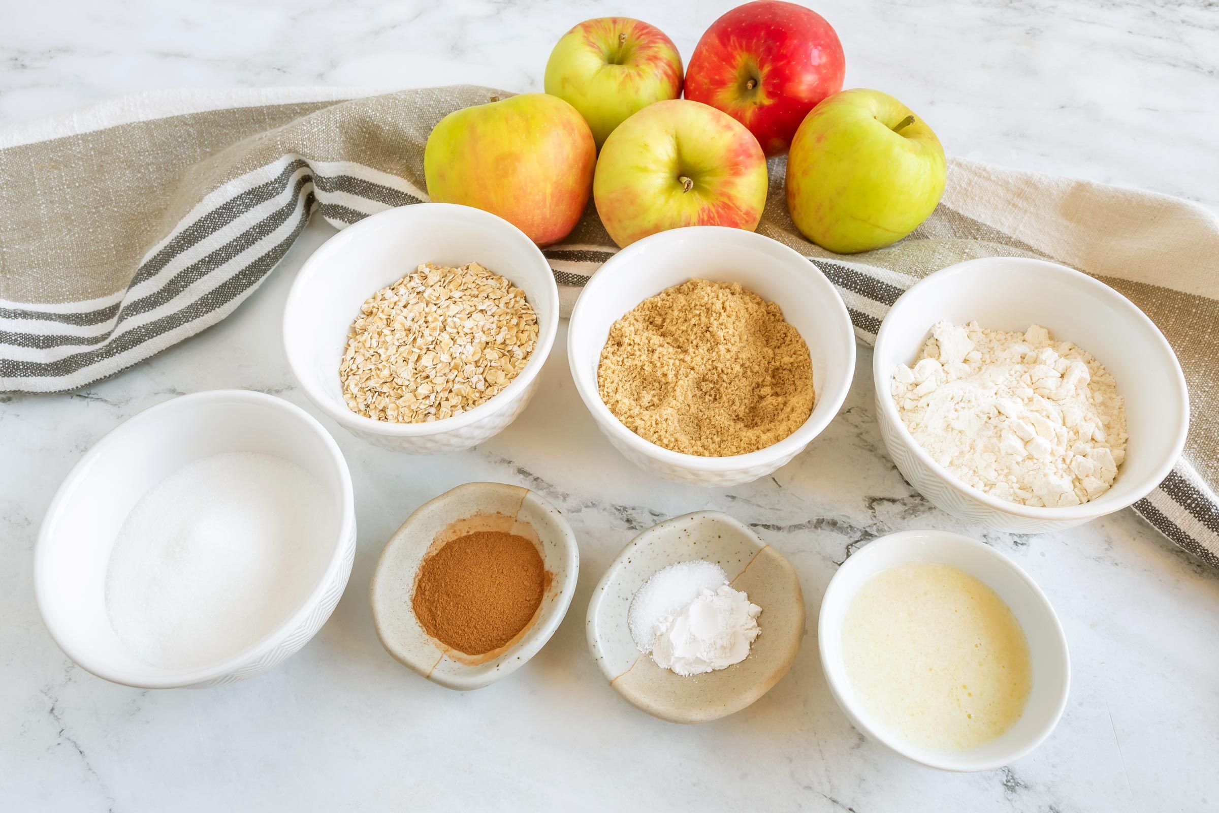 various small white bowls with measured out ingredients for amish apple goodie