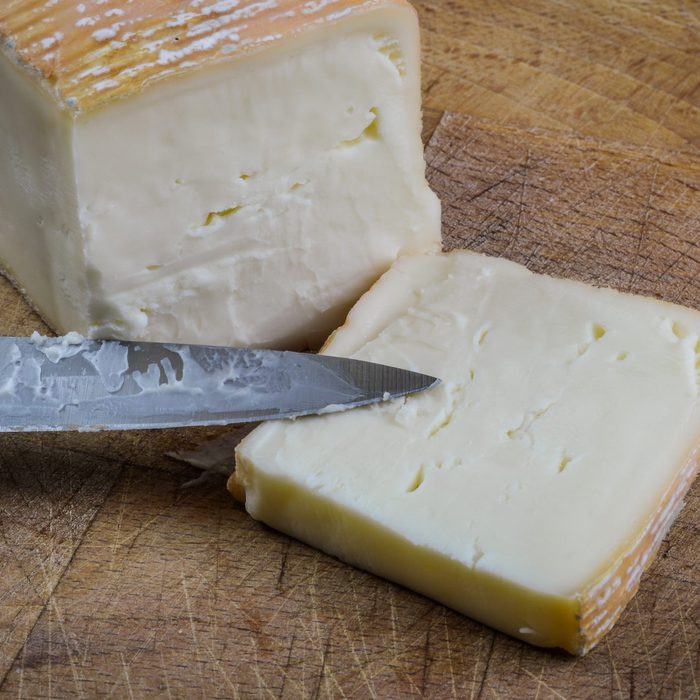 Piece of sliced taleggio italian cheese on a wooden cutting board with knife close up.