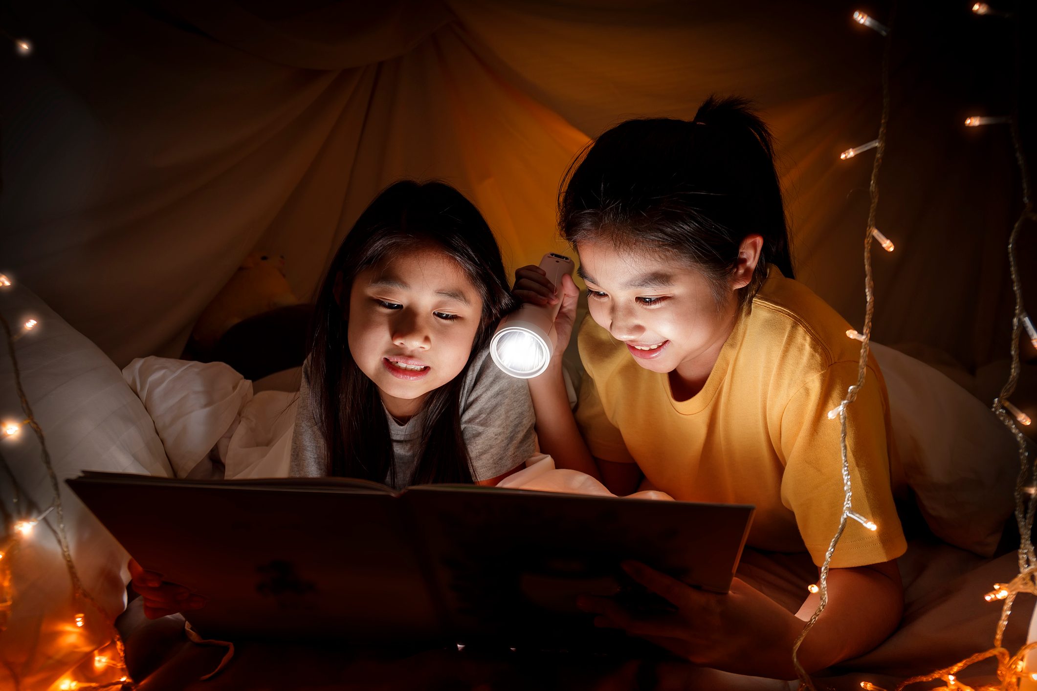 two friends using a flashlight and telling stories in a fort