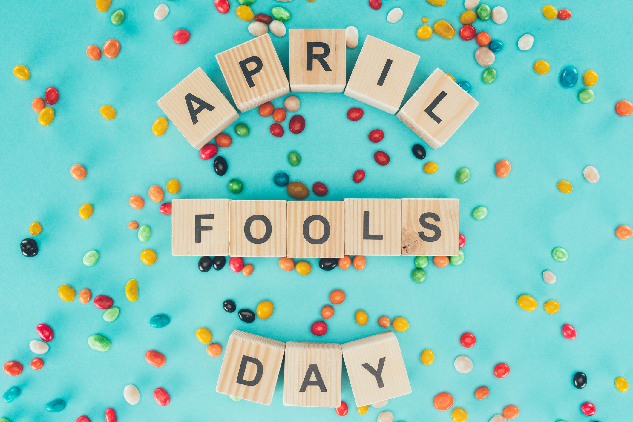 top view of arranged wooden cubes in april fools day lettering on blue surface with candies, 1 april holiday concept