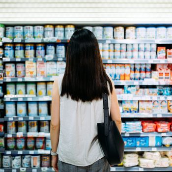 Rear view of young Asian mother groceries shopping for baby products in a supermarket