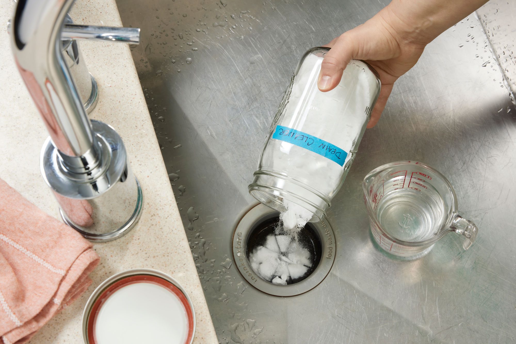Sink With Hand Pouring homemade drain cleaning Mixture From a glass jar into the drain