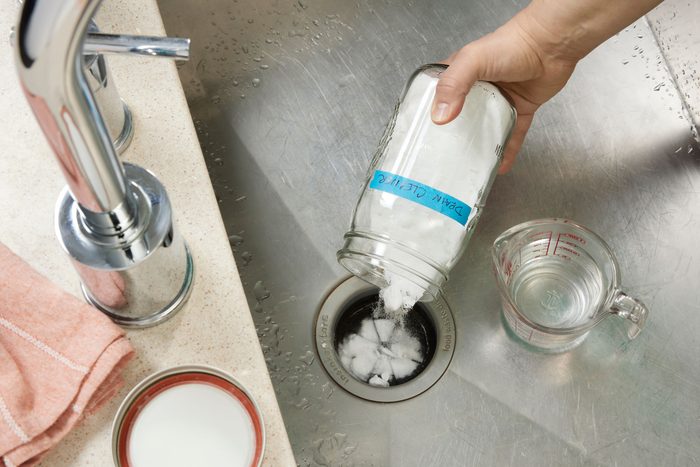 Sink With Hand Pouring homemade drain cleaning Mixture From a glass jar into the drain
