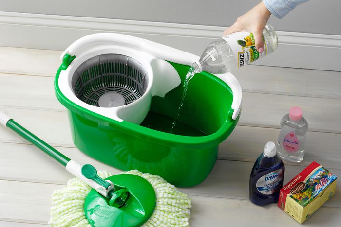 hand pouring vinegar into a mop bucket. mop and other supplies for homemade floor cleaner are arranged nearby