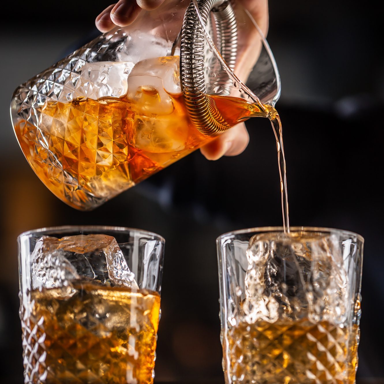 Whisky bourbon on ice being prepared by a professional bartender pouting the drink into ornamental glasses.