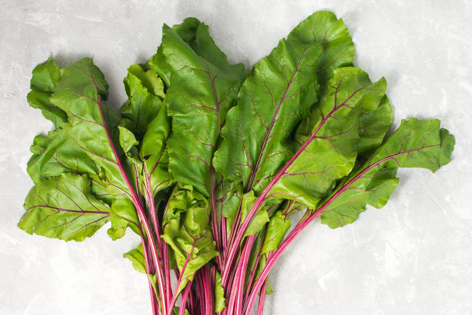 Some raw red beetroot with leaves on grey stone background. Square
