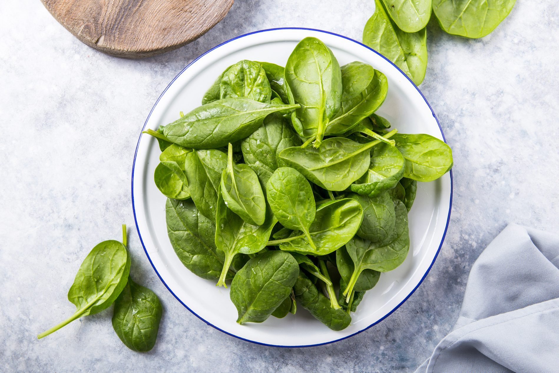 Baby spinach leaves in bowl on grey concrete background, top view, copy space. Clean eating, detox, diet food ingredient