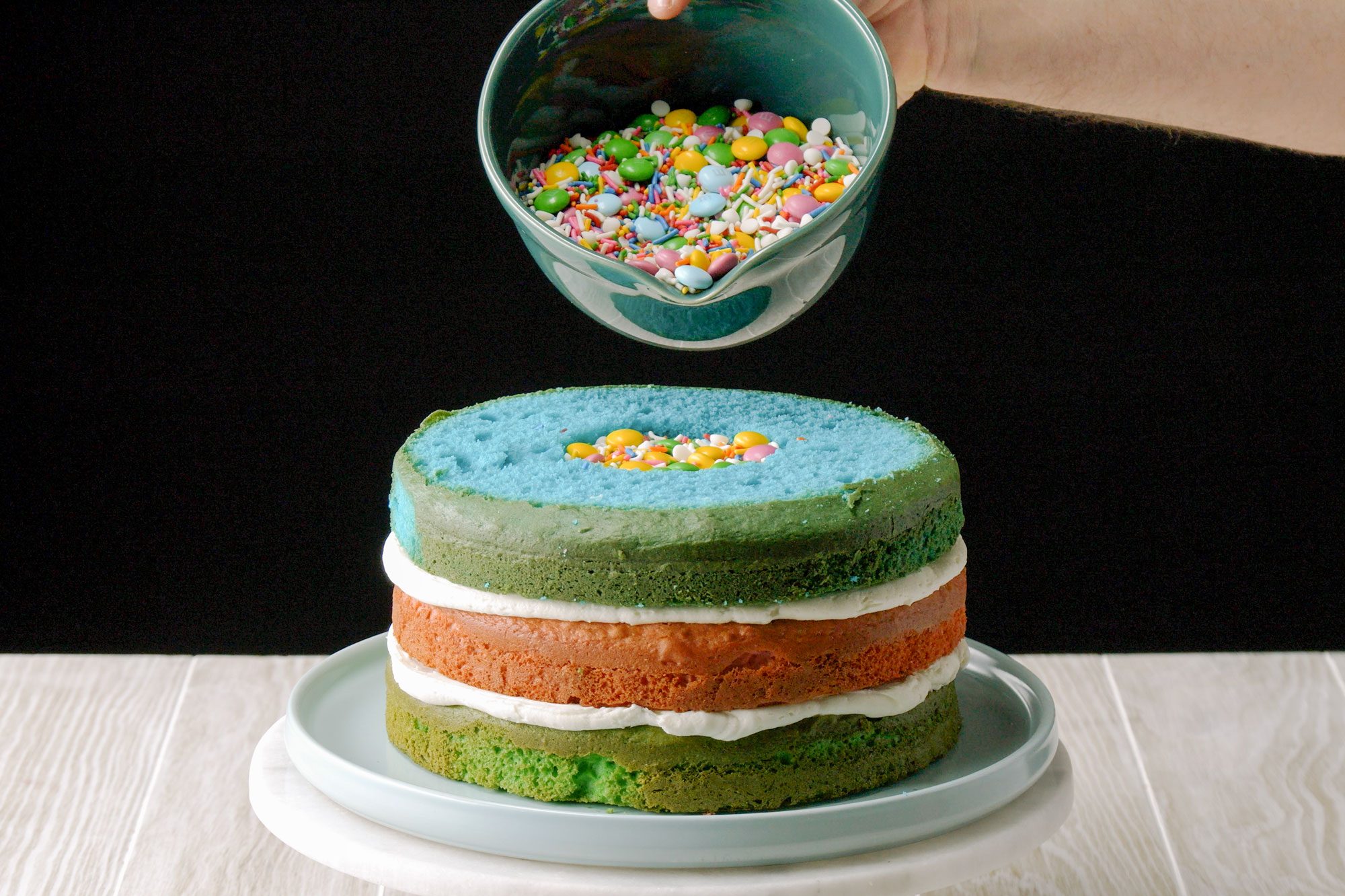 Hands filling surprise cake layers with sprinkles