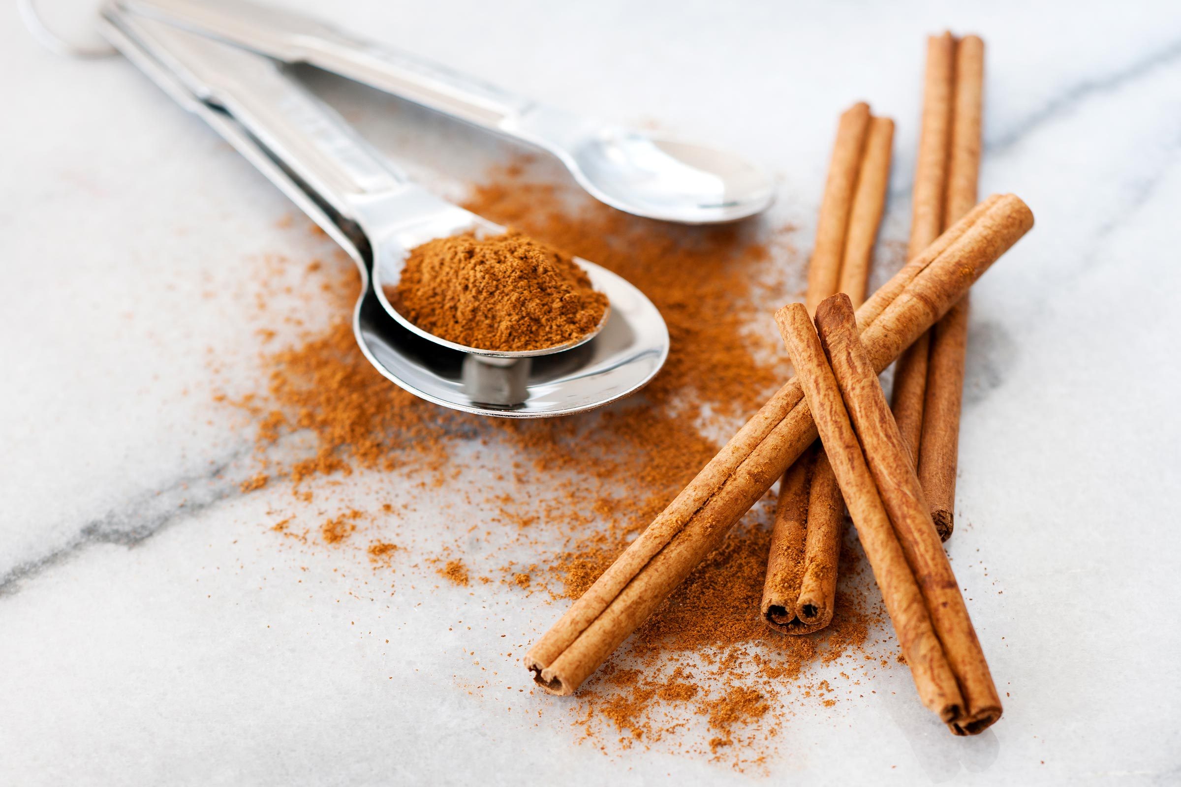 ground cinnamon on a metal spoon and cinnamon sticks
