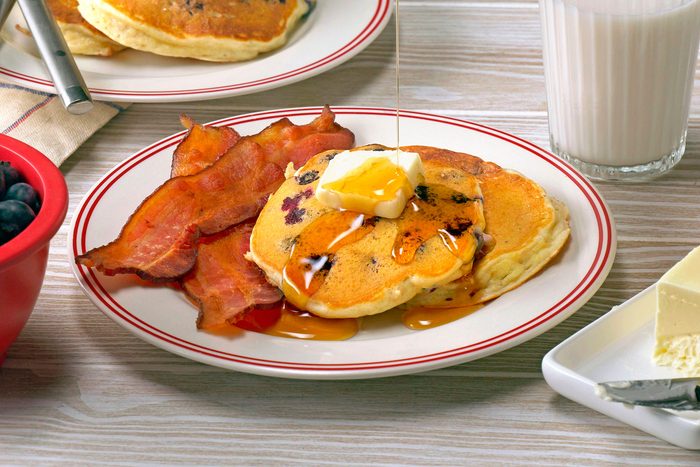 Blueberry Pancake served with bacon, butter and drizzled maple syrup on it with glass of milk