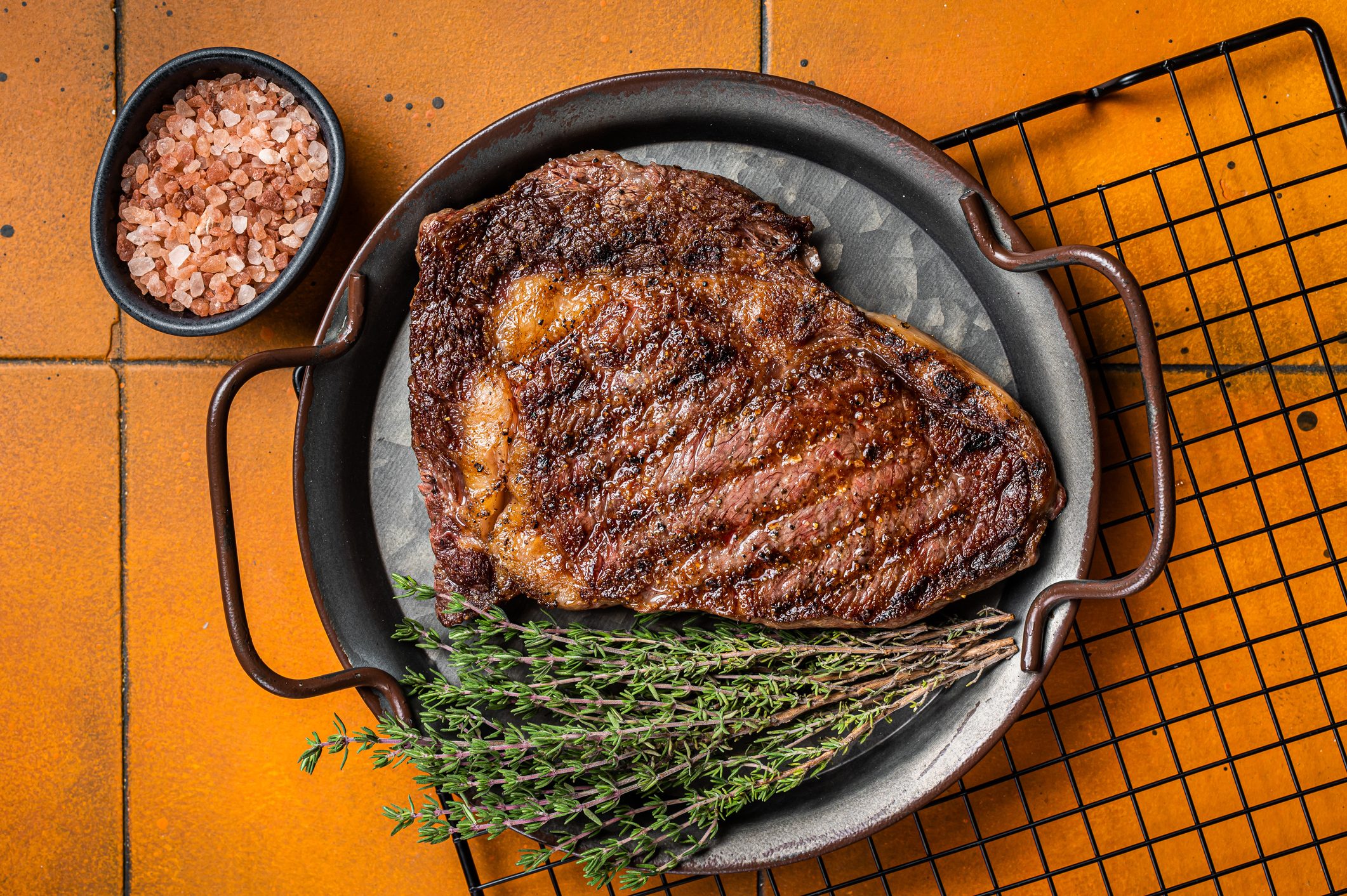 BBQ Grilled wagyu Rib Eye beef meat steak with herbs in steel tray. Orange background. Top view