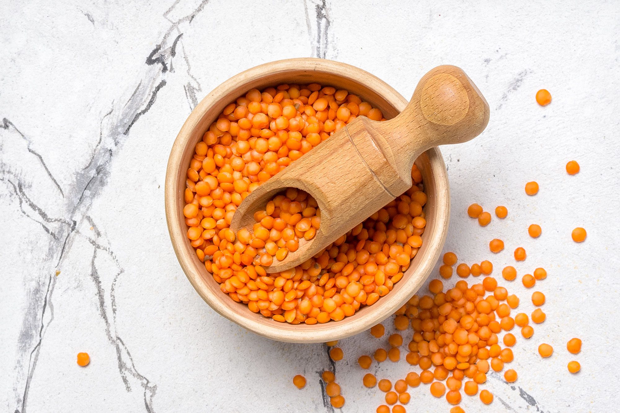Top View Of Raw Red Lentils In Bowl With Wooden Scoop On White Marble Background
