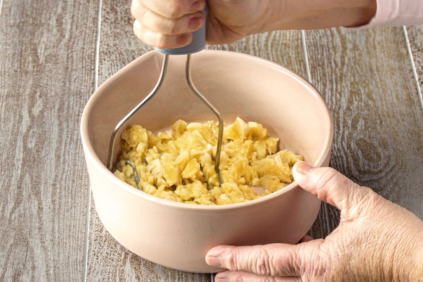 Mashing the bananas in a large bowl on a a wooden table