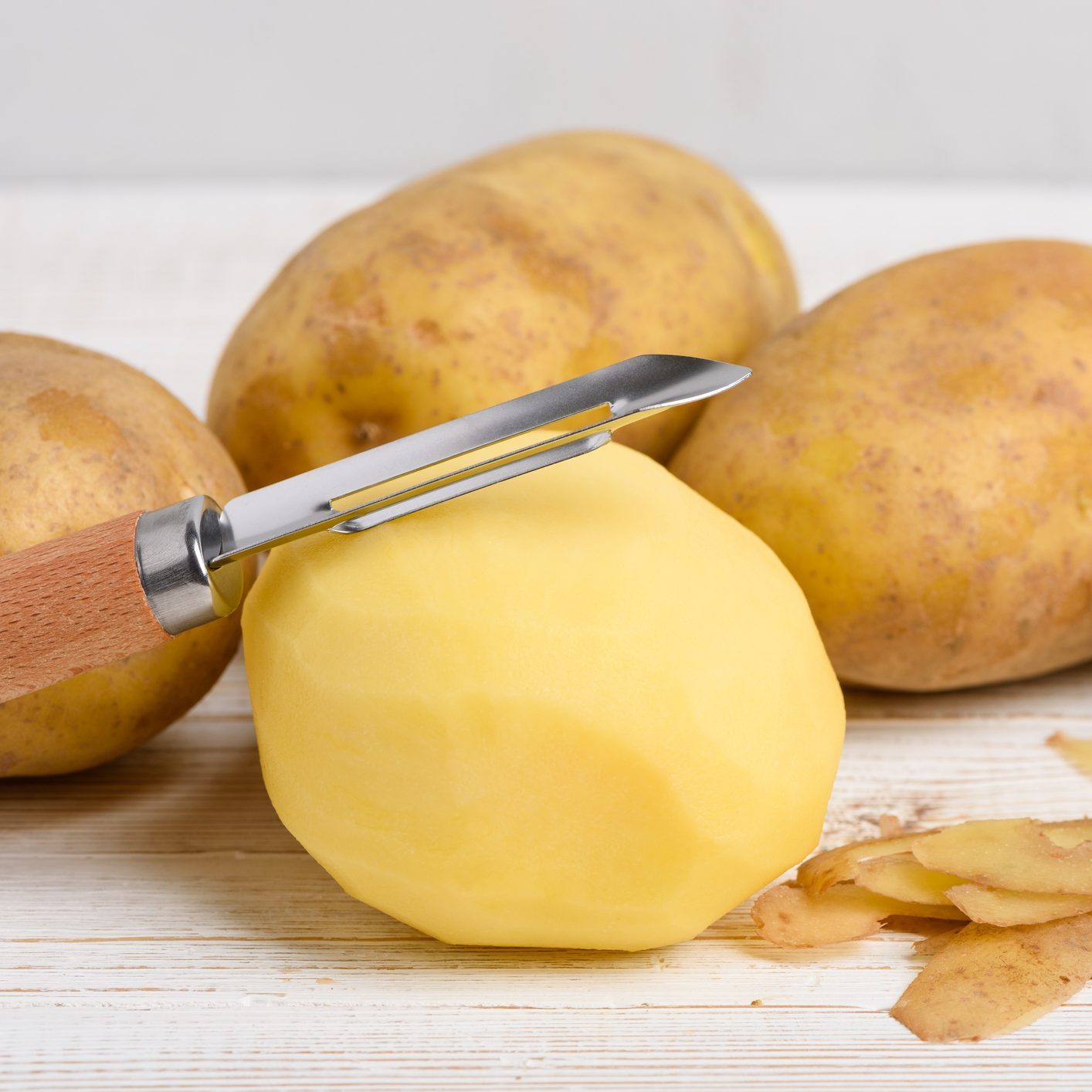 Raw peeled potato with vegetable peeler on wooden table
