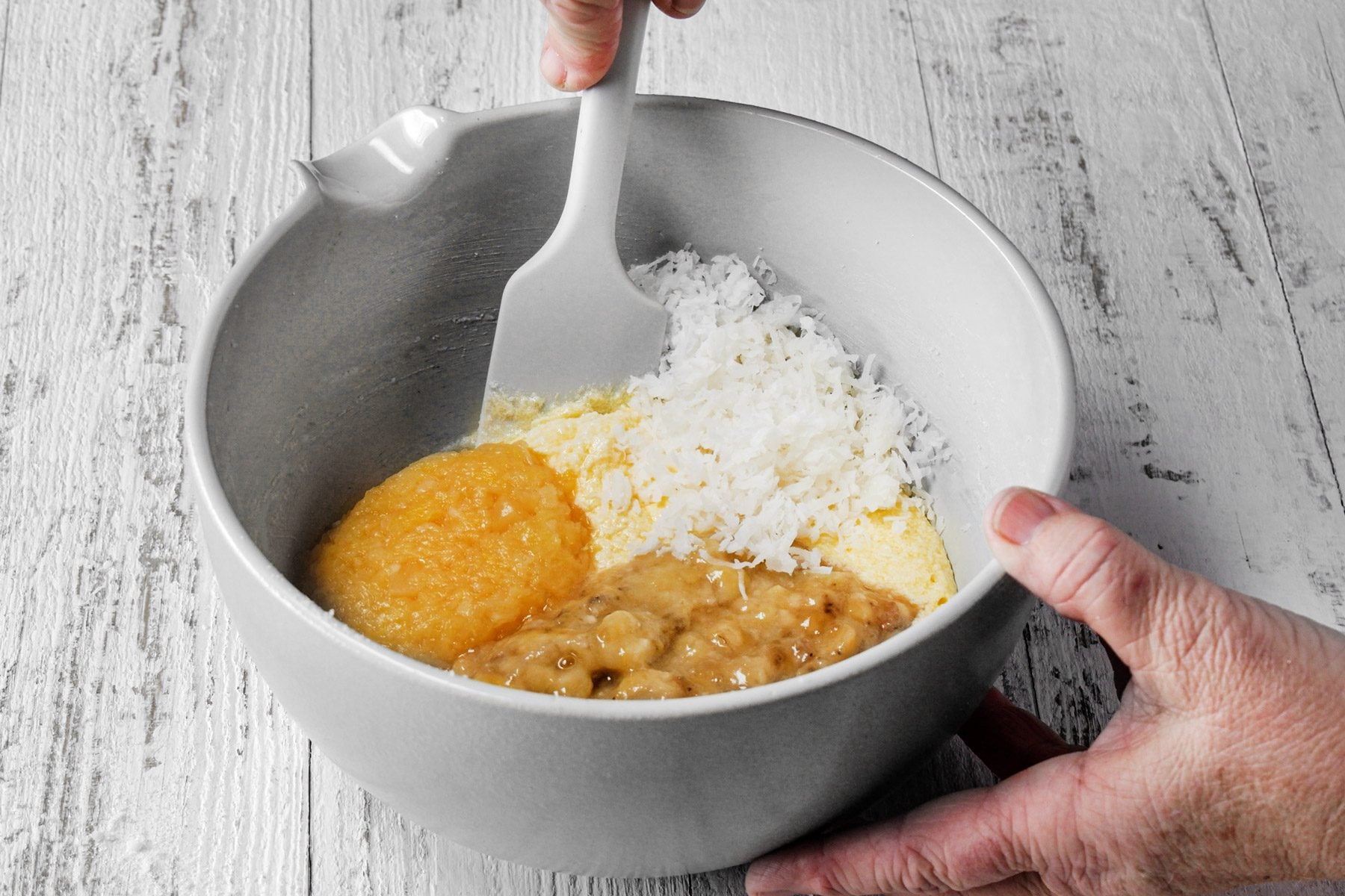 A person mixing the mashed bananas, crushed pineapple and shredded coconut