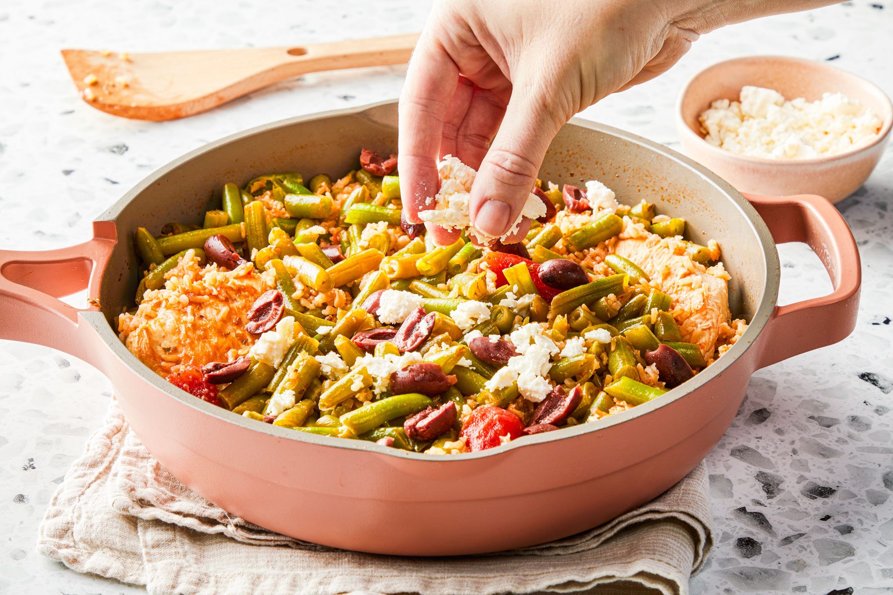 Garnishing feta cheese on Mediterranean Chicken in a large pan