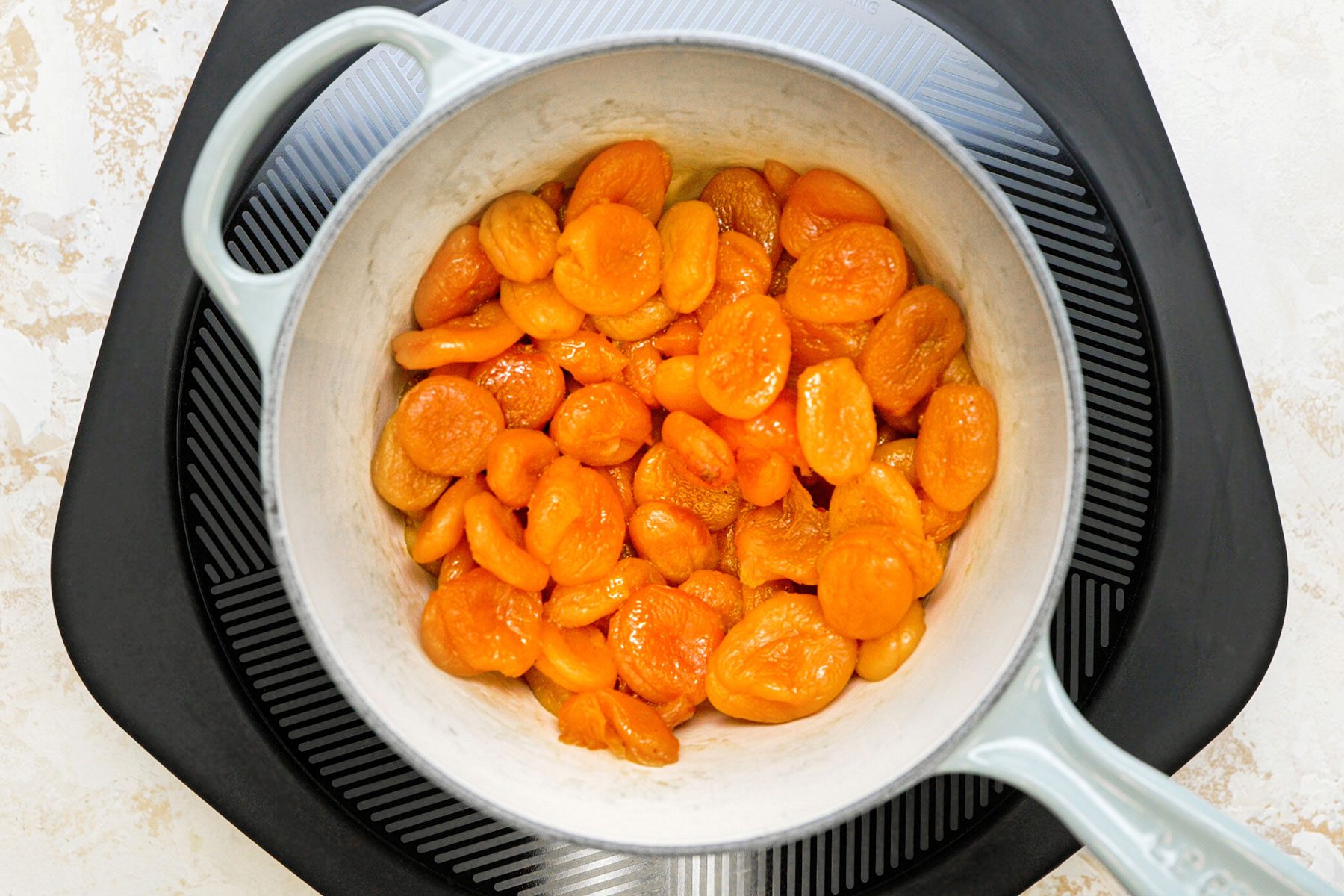 Cooking the apricots in a large saucepan on a marble countertop.