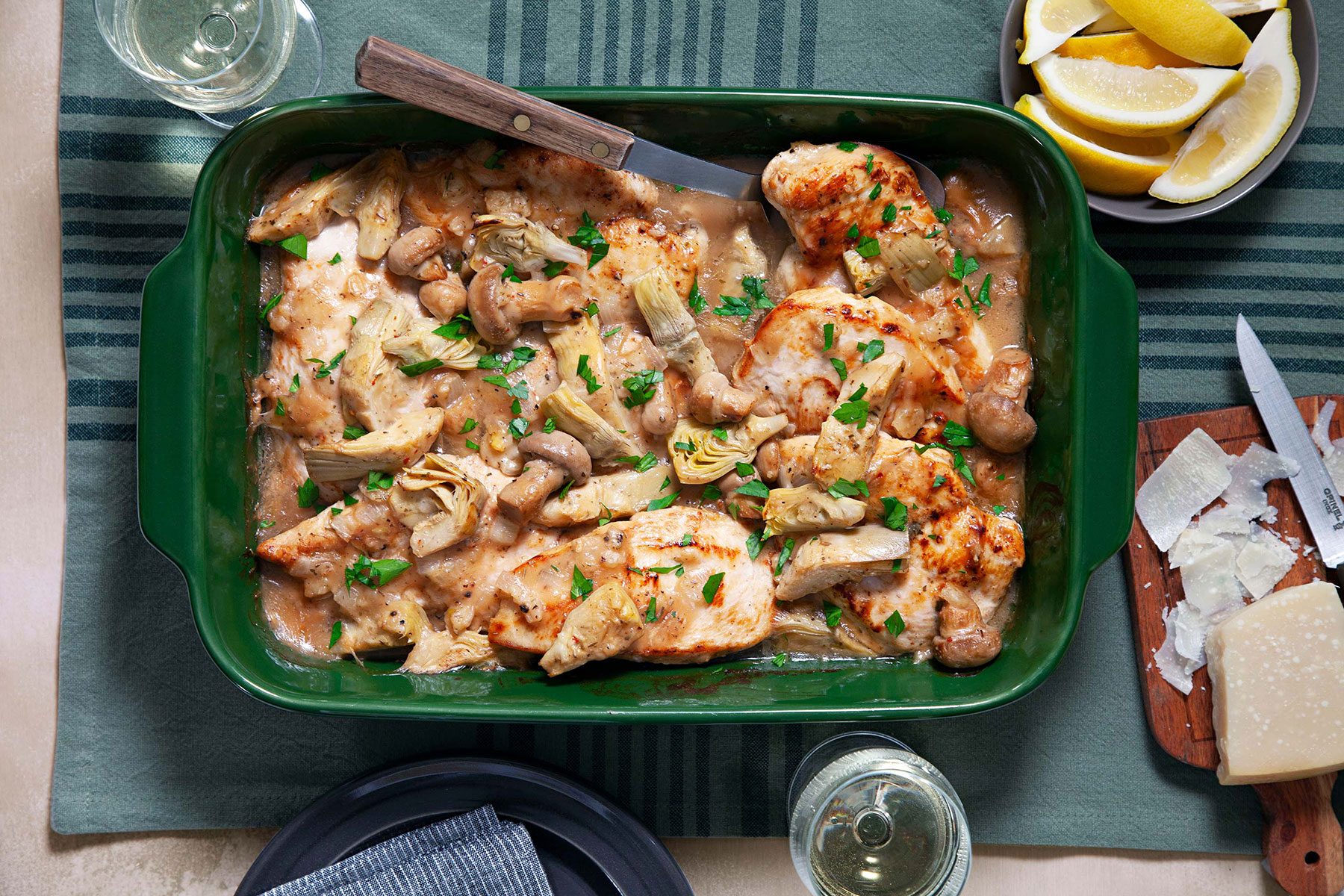 Artichoke Chicken served in serving dish with cheese and lemon wedges and drinks