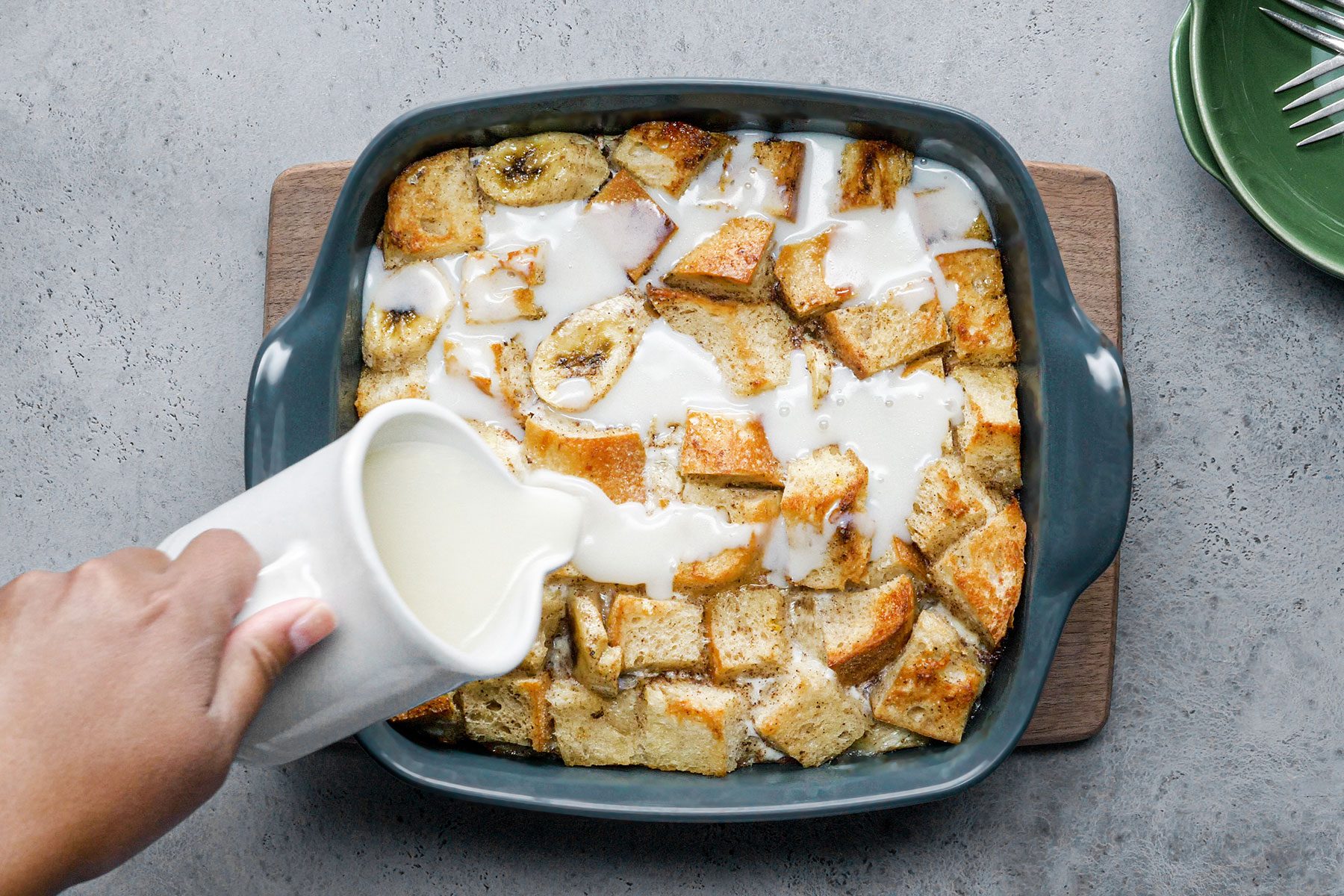 Pouring warm sauce over baked banana bread pudding