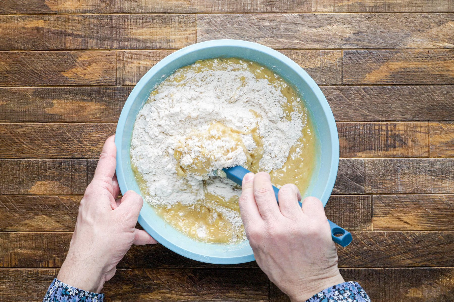Stirring dry ingredients into the wet ingredients using a spatula in a large bowl