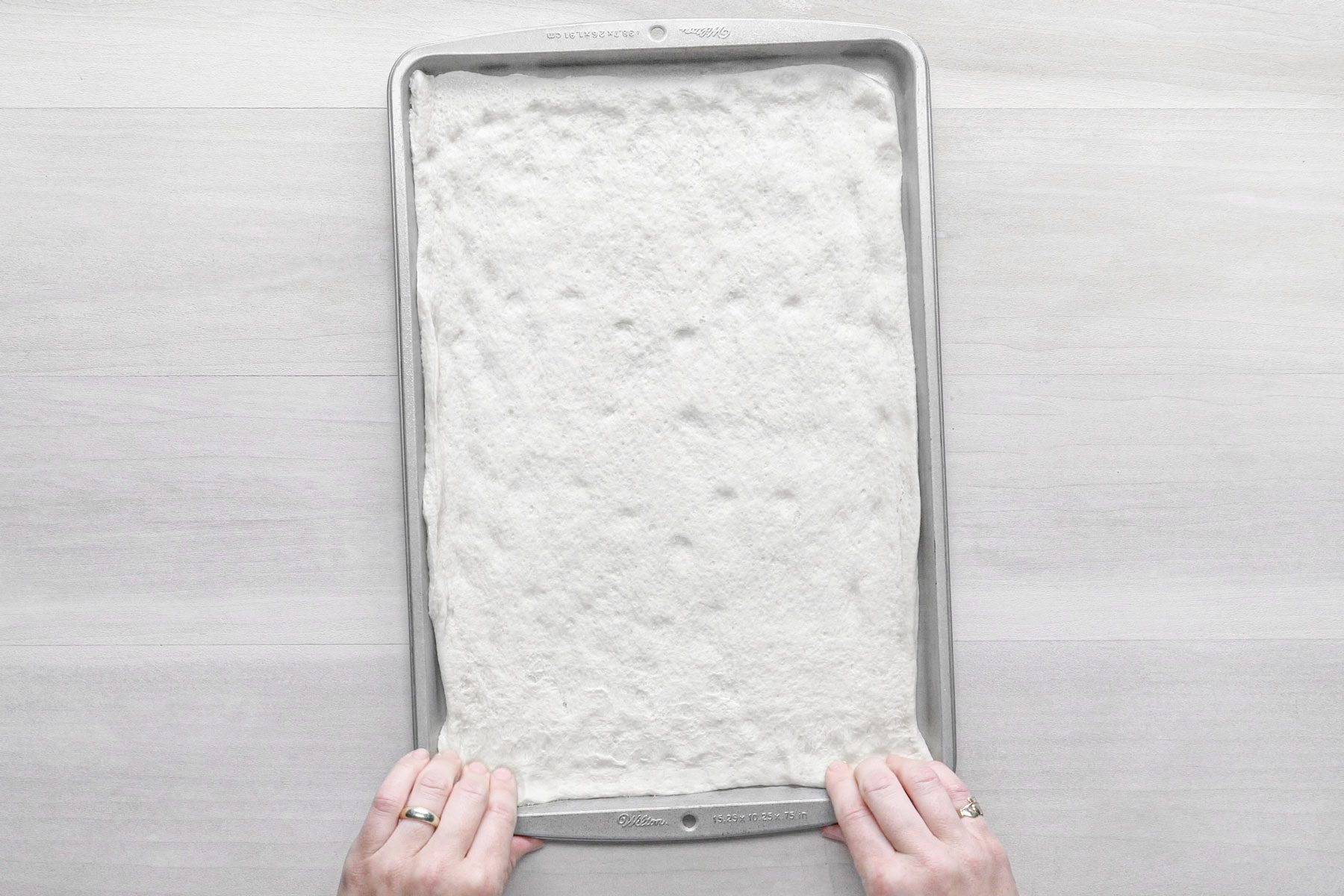 Pizza crust unrolled on a baking pan on a wooden surface