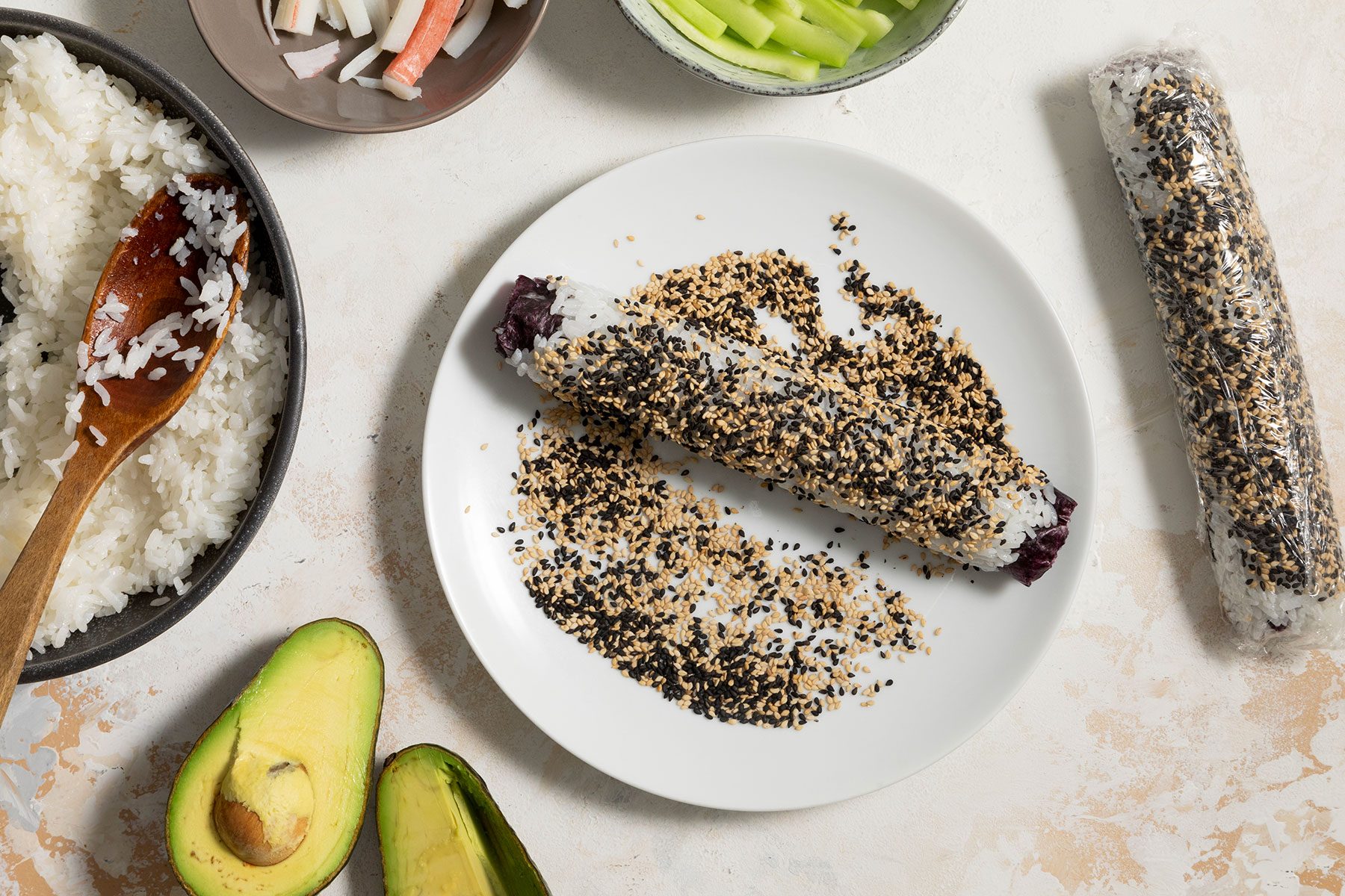 Rolling the sushi roll in sesame seeds spread on plate